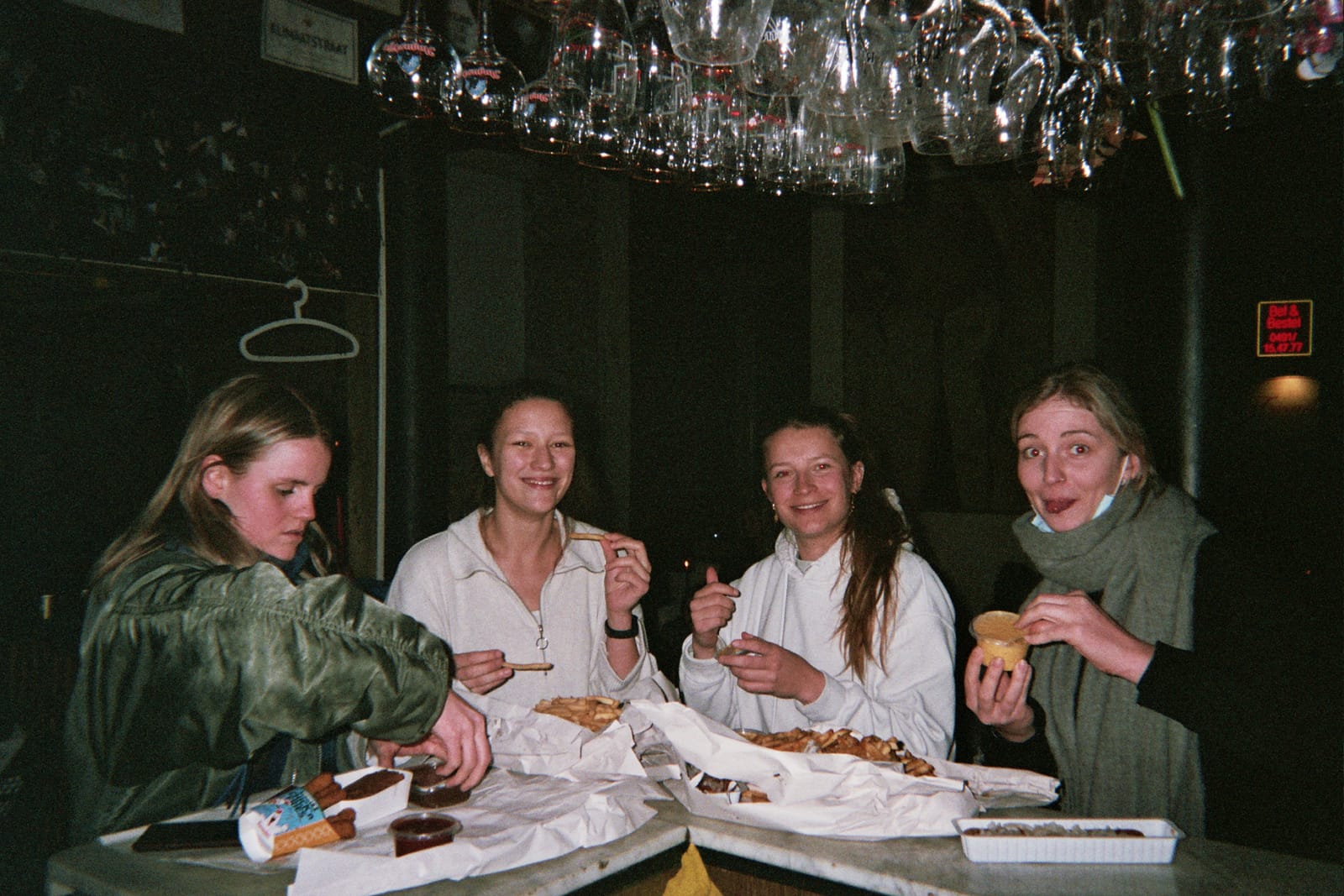 Vier mensen eten meegebracht eten aan een tafel in het café, onder de glazenrekken.